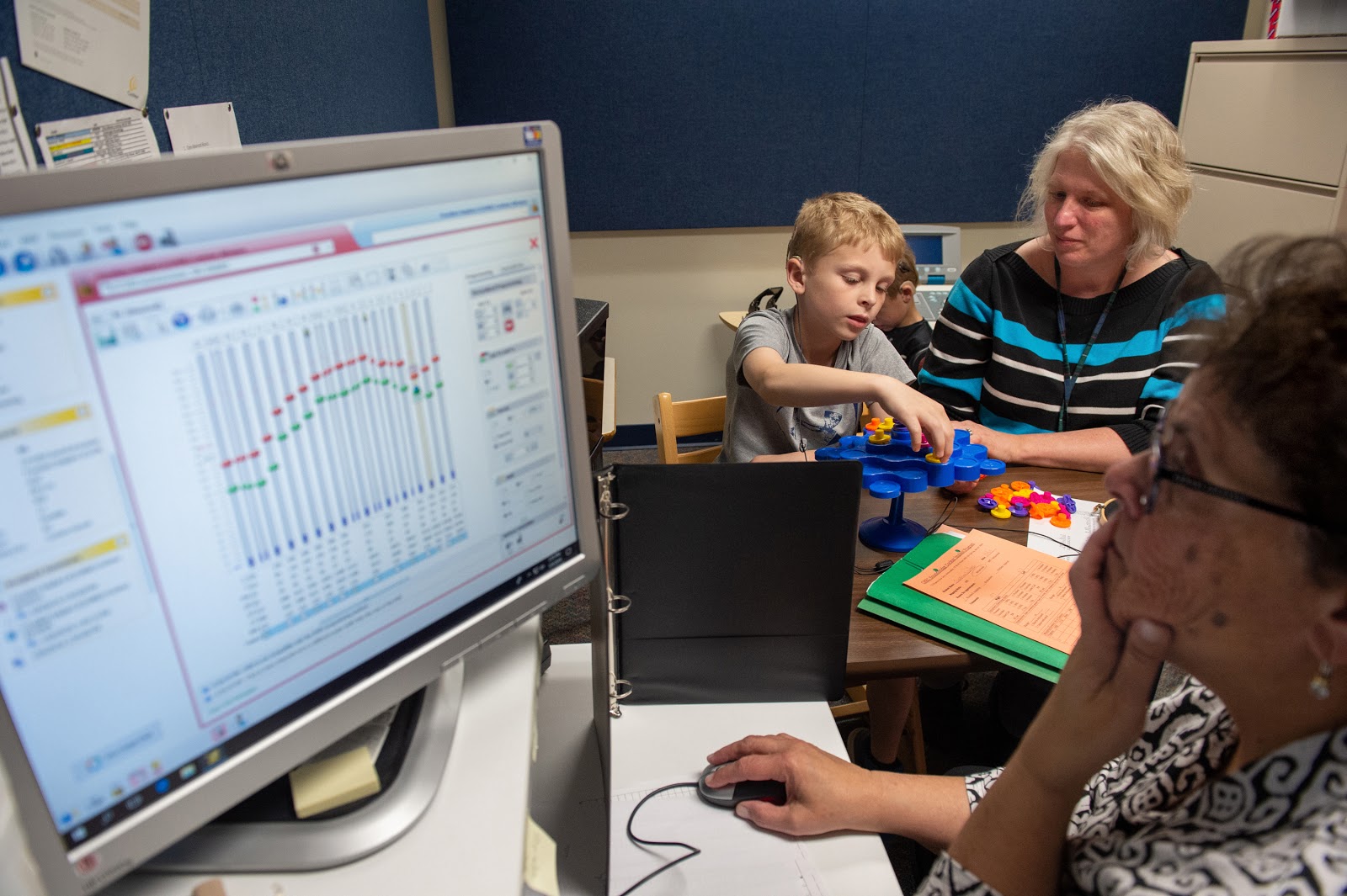 Resources for Parents On Gestural Communication 3 From WNPR: Raisa Usifer, (right, foreground) an audiologist, tests Chase Walters’ hearing during a cochlear implant mapping session at CREC Soundbridge in Wethersfield recently. Hearing impaired teacher Ruth Ennis (right, background) works with Chase. Chase and his brother, Jackson, both born with hearing loss, get their implants mapped twice a year to make sure they are properly adjusted. (Photo credit: Cloe Poisson)